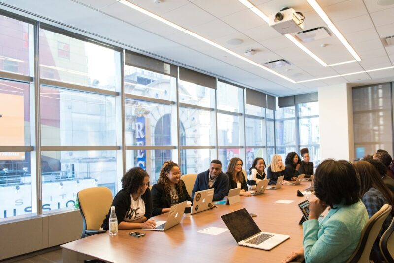group of people sitting beside rectangular wooden table with laptops